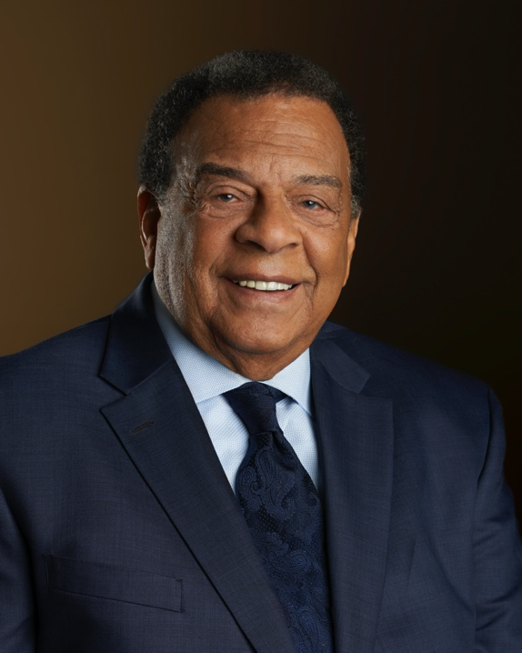 Ambassador Andrew Young, an older African American Male, smiles wearing a navy suit with a light blue collared shirt and a navy blue tie with a floral pattern.